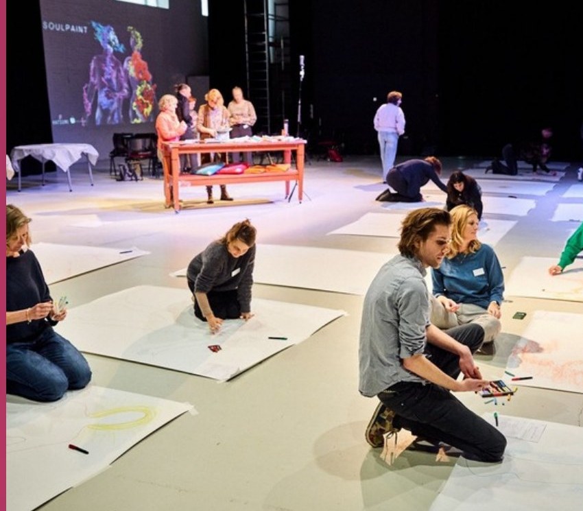 Mensen tekenen op grote vellen papier op de vloer tijdens een body mapping workshop