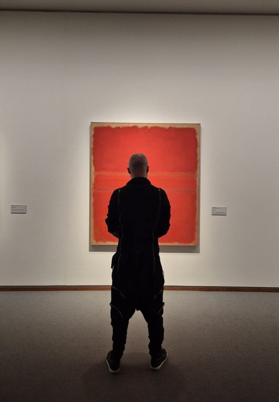 Iemand staat in een museum voor een groot rood schilderij van Mark Rothko
